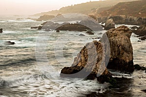 Oceanside shoreline with rocks in water at sunset