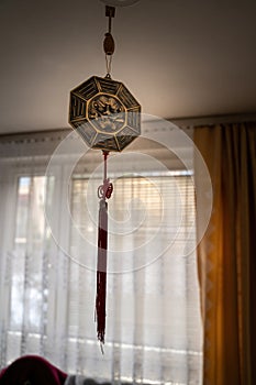 Octagon Bagua Mirror Feng Shui hanging from a roof inside a room against curtains- powerful cure to protect against negative