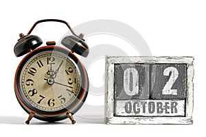 October 02 on wooden calendar with alarm clock white background.