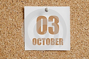 october 03. 03th day of the month, calendar date.White calendar sheet attached to brown cork board.Autumn month, day of