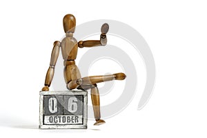 October 06, wooden calendar with mannequin sitting on it on white background. Calendar date.