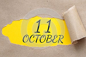 october 11. 11th day of the month, calendar date.Hole in paper with edges torn off. Yellow background is visible through