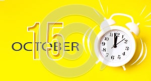 October 15th. Day 15 of month, Calendar date. White alarm clock with calendar day on yellow background. Minimalistic concept of