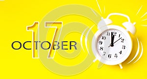 October 17th. Day 17 of month, Calendar date. White alarm clock with calendar day on yellow background. Minimalistic concept of