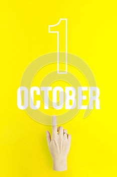 October 1st . Day 1 of month, Calendar date.Hand finger pointing at a calendar date on yellow background.Autumn month, day of the