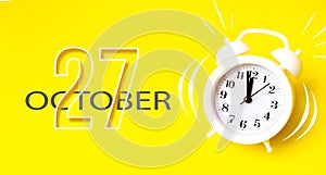 October 27th. Day 27 of month, Calendar date. White alarm clock with calendar day on yellow background. Minimalistic concept of