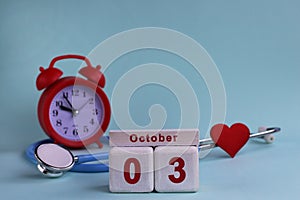 October 3. Day of the 3th month, calendar date. White wooden calendar blocks with date, clock and stethoscope on blue pastel