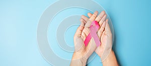 October Breast Cancer Awareness month, adult Woman  hand holding Pink Ribbon on blue background for supporting people living and