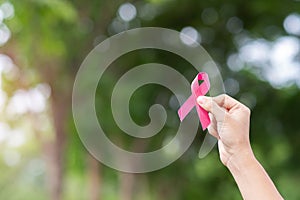 October Breast Cancer Awareness month, adult Woman  hand holding Pink Ribbon with green background for supporting people living