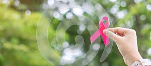 October Breast Cancer Awareness month, adult Woman  hand holding Pink Ribbon with green background for supporting people living