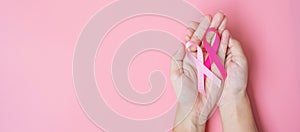 October Breast Cancer Awareness month, adult Woman hand holding Pink Ribbon on pink background for supporting people living and