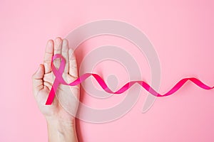 October Breast Cancer Awareness month, adult Woman hand holding Pink Ribbon on pink background for supporting people living and
