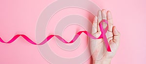 October Breast Cancer Awareness month, adult Woman hand holding Pink Ribbon on pink background for supporting people living and