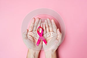 October Breast Cancer Awareness month, adult Woman hand holding Pink Ribbon on pink background for supporting people living and