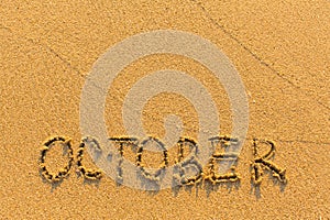 October - word inscription on the gold sand beach.