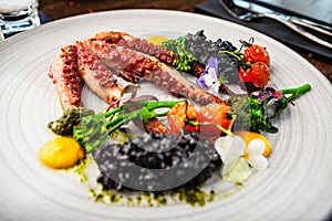 Octopus with black risotto. Carrot cream, mini-broccoli, basil pesto. Delicious healthy traditional food closeup served
