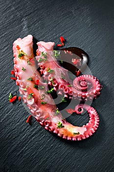 Octopus serving with vegetables, sea food. Freshly boiled curved octopus tentacles dish on a dark