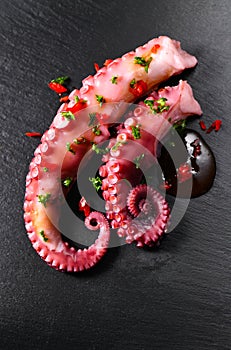 Octopus serving with vegetables, sea food. Freshly boiled curved octopus tentacles dish on a dark stone