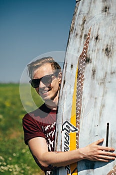 ODESSA, UKRAINE - MAY, 20 2015: Young hipster man surfer with an old surfboard is on way to the beach. Close up portrait