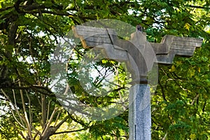 An off-centered shot of an old, bird shaped, outdoor, cement lighting post., with a wide wing span, located in a Thai public park.