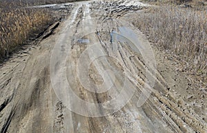 Off-piste. Deep rubber tracks on the road is covered with wet dirty sand, off-road. Traces of tires in the dirt. Impassable road