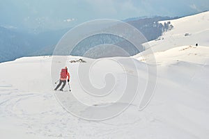 Off piste skier, wearing colorful red clothes, descending on a ridge in Baiului mountains, Romania, towards the foggy forest