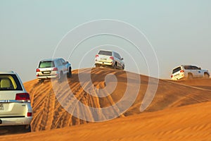 Off-road adventure with SUVs driving in Arabian Desert at sunset. Traditional entertainment for tourists with vehicle bashing thro