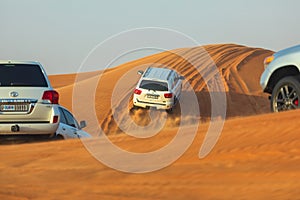 Off-road adventure with SUVs driving in Arabian Desert at sunset. Traditional entertainment for tourists with vehicle bashing thro