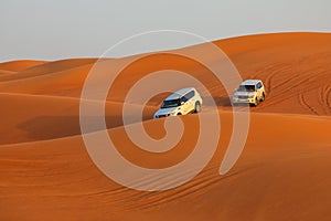 Off-road adventure with SUVs driving in Arabian Desert at sunset. Traditional entertainment for tourists with vehicle bashing thro