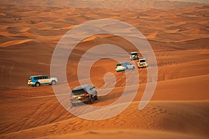 Off-road adventure with SUVs driving in Arabian Desert at sunset. Traditional entertainment for tourists with vehicle bashing thro