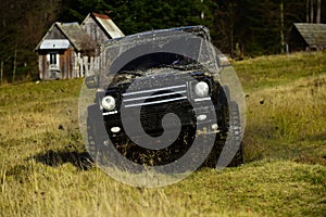 Off road car in black color takes part in racing. Cross country rallying or rally raid near countryside hut aside forest