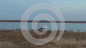 Off road car driving on dirt route on autumn field on lake and forest landscape. Drone view crossover car traveling along river sh