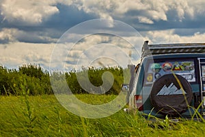 Off-road car is moving among tall green grass against a beautiful sky background