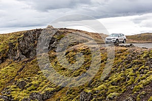 Off-road car parked at the edge of the volcanic cliff overgrown with moss in Gjain canyon, Iceland