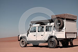 Off-road car stands in the red sands of the Namib Desert on a sunny day.  Sossusvlei, Namibia