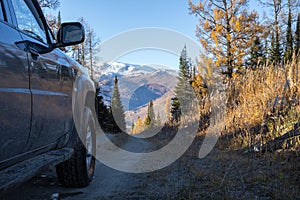 Off-road travel on mountain road in autumn. Black SUV on mountain road with mountains covered with snow on the background.