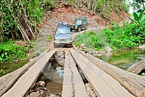 Off road vehicles are crossing the creek by a wooden bridge in the forest