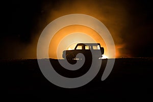 Off roader jeep silhouette on dark toned foggy sky background. Car with light at night.