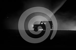 Off roader jeep silhouette on dark toned foggy sky background. Car with light at night.