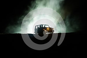 Off roader jeep silhouette on dark toned foggy sky background. Car with light at night.