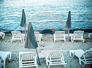 Off season on the sand beach with no people. Closed sun umbrellas, parasol, white plastic chairs, couches