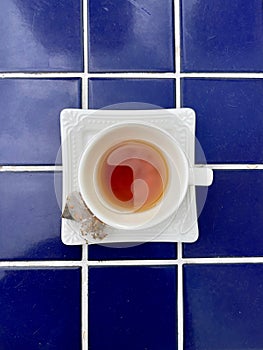 An off white porcelain cup and saucer with delicious herbal tea on a blue tile