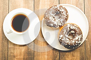 Ð¡offee break. White cup with black coffee and donat in chocolate glaze. Wooden background, top view