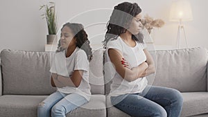 Offended african american mother and daughter sitting back to back on sofa, looking angrily at each other