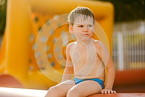 Offended boy in swimming trunks on the beach. sad three-year-old child sitting on an inflatable football pool