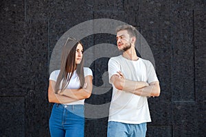 Offended Caucasian man and woman looking at each other and standing in white T-shirts with arms