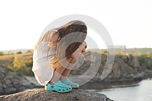 Offended five-year-old sad girl sitting on rocks in nature alone.