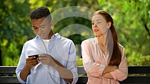 Offended girlfriend looking at boyfriend chatting on smartphone, unfaithful