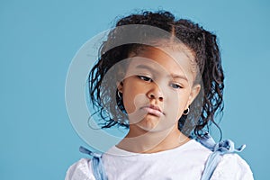 Offended little hispanic girl looking sad and upset while posing against a blue studio background. Unhappy preschooler