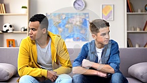 Offended multiracial teen boys sitting looking different directions, conflict